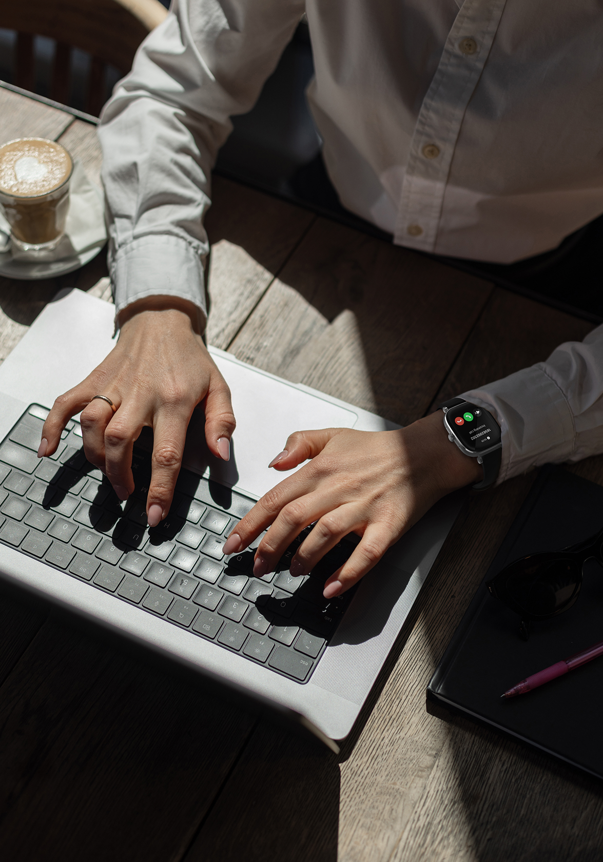 Person typing on a laptop wearing smartwatch with a cup of coffee and notebook in the background